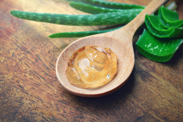 Aloe vera gel on wooden spoon with aloe vera leaves on wooden board.
