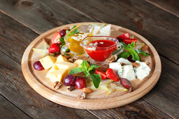 Fruits and cheese oh catering platter top view. Wooden board with variety of cheese and fruits with red and yellow sauces on dark wooden background. Wine snack set