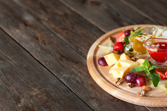 Cheese with grapes and sauces on wood copyspace. Catering platter with gouda cheese, grapes and red and yellow sauces, decorated with mint and nuts