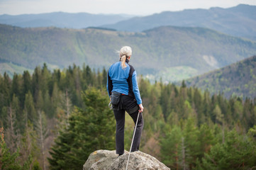 Climber woman in a blue jacket with climbing equipment standing with back to camera on the top of...