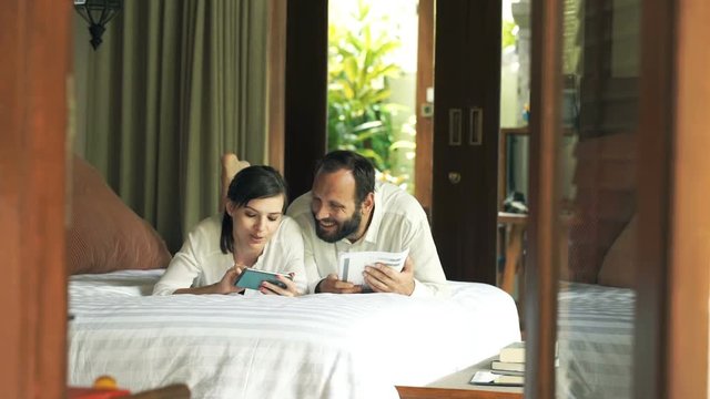 Young couple sitting with smartphone and documents in the bedroom
