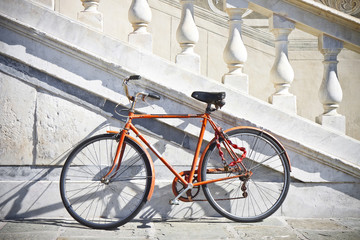 Fototapeta na wymiar Orange old bicycle against a marble wall (Tuscany - Italy)