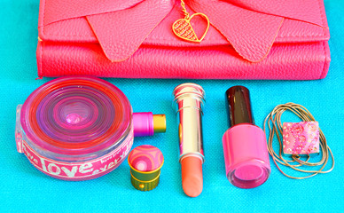 Naklejka premium Women accessories - pink clutch,lipstick,nail polish,perfume bottle,necklace on a turquoise background. Cosmetic products background.Selective focus.