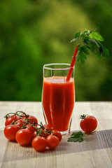 A glass of tomato juice, lying next to a branch of tomatoes