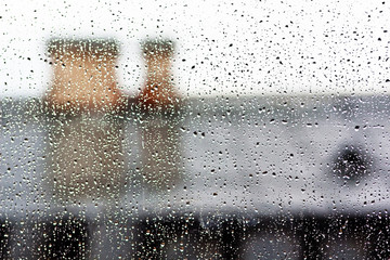 Stream of water in heavy rain. Raindrops on window pane. Blur effect. Old roof.