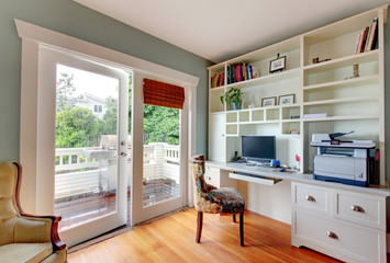Home office with white open shelves, desk and hardwood floor.