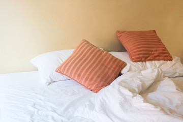white pillow and orange pillow on bed and with wrinkle messy bla