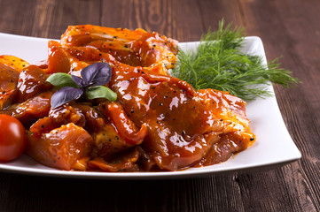 Pieces of raw pork on white plate. Chunks of barbecue in a sauce. Pieces of raw pork in barbecue sauce on a white plate with tomato basil dill.