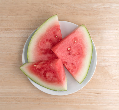 Sections of watermelon on a plate top view atop a wood table illuminated with natural light.