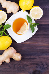Cup of tea with lemon, mint and ginger on a dark wooden table. Top view with copy space