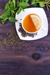 Cup of green tea with lemon and mint leaves on a dark wooden background. Top view with copy space