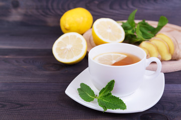 Cup of tea with lemon, mint and ginger on a dark wooden background