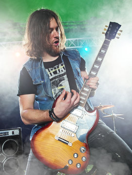 Rock band performs on stage. Guitarist, bass guitar and drums.
