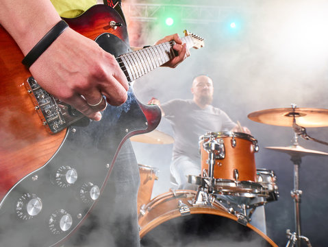 Rock band performs on stage. Guitarist and drums.