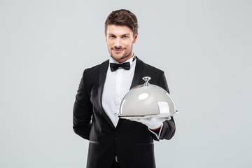 Smiling young butler holding tray with silver catering dome