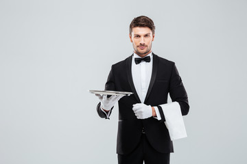 Attractive butler in tuxedo standing and holding silver empty tray