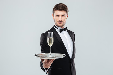Attractive young butler in tuxedo offers you glass of champagne