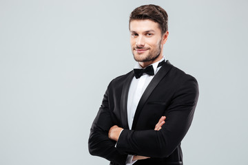 Smiling confident man in tuxedo standing with arms crossed