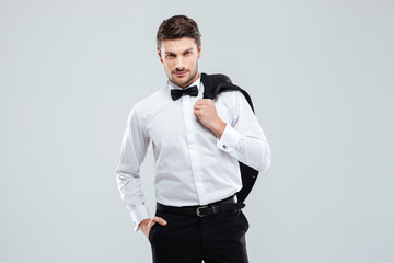 Gorgeous young man in tuxedo standing and holding his jacket