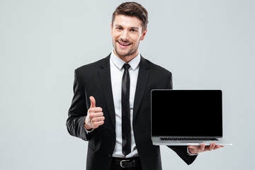 Cheerful businessman holding blank screen laptop and showing thumbs up