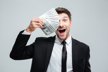 Funny excited young businessman covered one eye with money