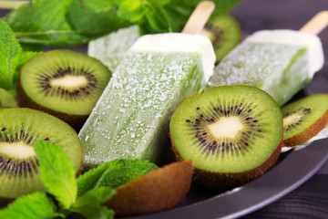 Fototapeta na wymiar Homemade kiwi popsicles on a plate with mint and kiwi slices on a dark wooden background