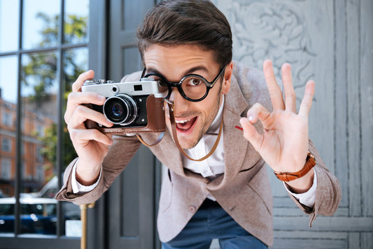 Happy funny male photographer in round glasses taking pictures outdoors