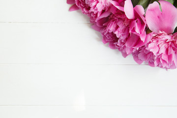 Bright pink peonies on white wooden background. Fresh summer floral background with copy space. Top view, flat lay
