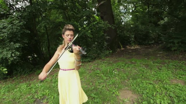 Female classical musician plays electric violin outdoors; steadicam shot; real people; 