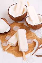 Homemade coconut popsicles on a paper with ice on a white wooden background