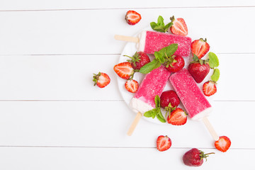 Homemade strawberry popsicles on a plate with mint on a white wooden background
