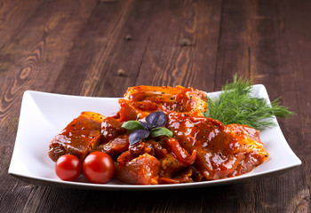 Pieces of raw pork on white plate. Chunks of barbecue in a sauce. Pieces of raw pork in barbecue sauce on a white plate with tomato basil dill.