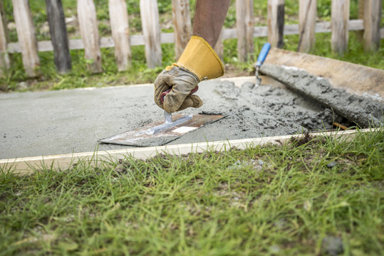 Man with protective gloves levelling the surface of a concrete p