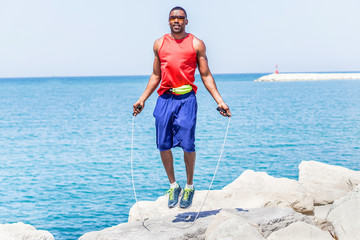 Black handsome man jumping rope with sea view in background 