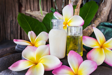 Mini set of bubble bath and shower gel liquid with pink white and yellow flowers plumeria or frangipani on timber or log and green leaf background,mini shampoo conditioner treatment 