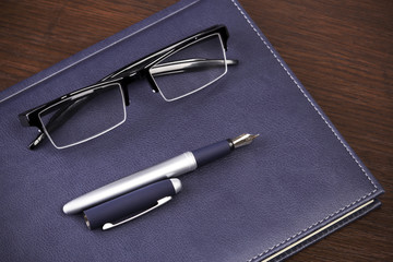 Business accessories on desktop: notebook, diary, fountain pen, cufflinks, glasses