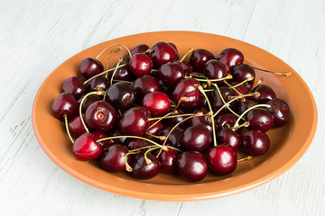 Sweet cherries .  Sweet cherries on a brown ceramic plate on a light wooden background.