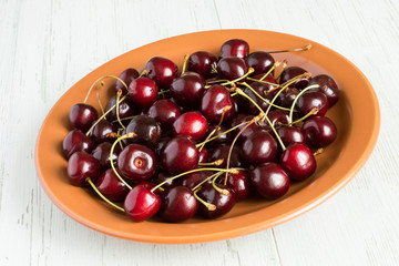 Sweet cherries .  Sweet cherries on a brown ceramic plate on a light wooden background.
