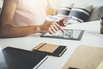Female hands using modern digital tablet and holding debit card to pay online, cozy bedroom in background, shopping concept, young hipster girl paying from home with credit card via portable tablet