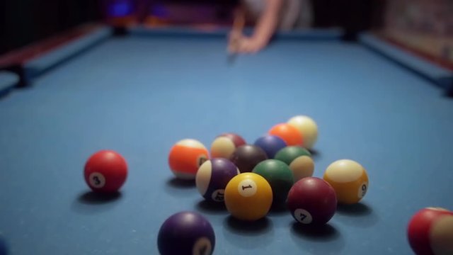 POV of pool break on a vintage worn out blue cloth pool table in slow motion. Sports game of billiards / 8 ball. Focus on the racked balls.
