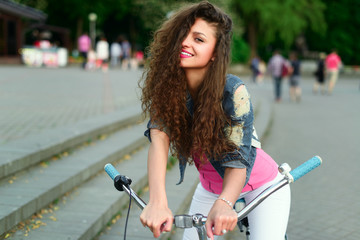 Fototapeta na wymiar Young and pretty girl with curly hair on a bike in the Park summer smiles