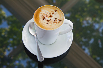 A cup of coffee in a white cup on glass background