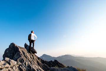 businessman success hiking on the peak of rocks mountain at sunset, success winner, leader concept
