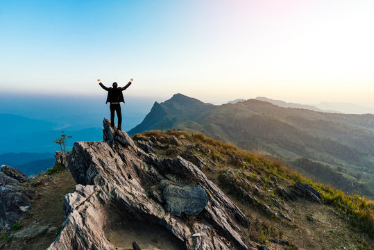 businessman success hiking on the peak of rocks mountain at sunset, success winner, leader concept