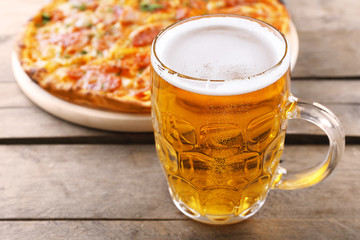 Tasty pizza and glass of beer are on wooden table, close up