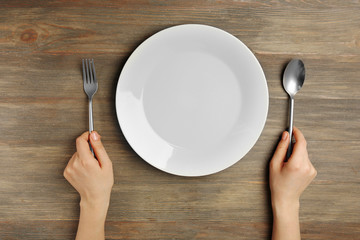 Female hands with cutlery and empty plate on wooden background