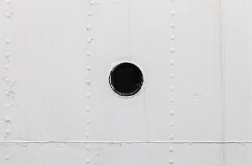 Small round rusted porthole in white ship hull