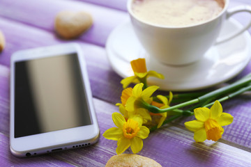 Cup of coffee with yellow daffodils on wooden background