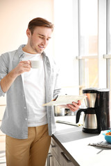 Young man making coffee and reading newspaper in kitchen