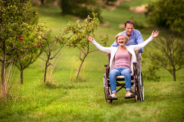 Senior man pushing woman in wheelchair, green autumn nature
